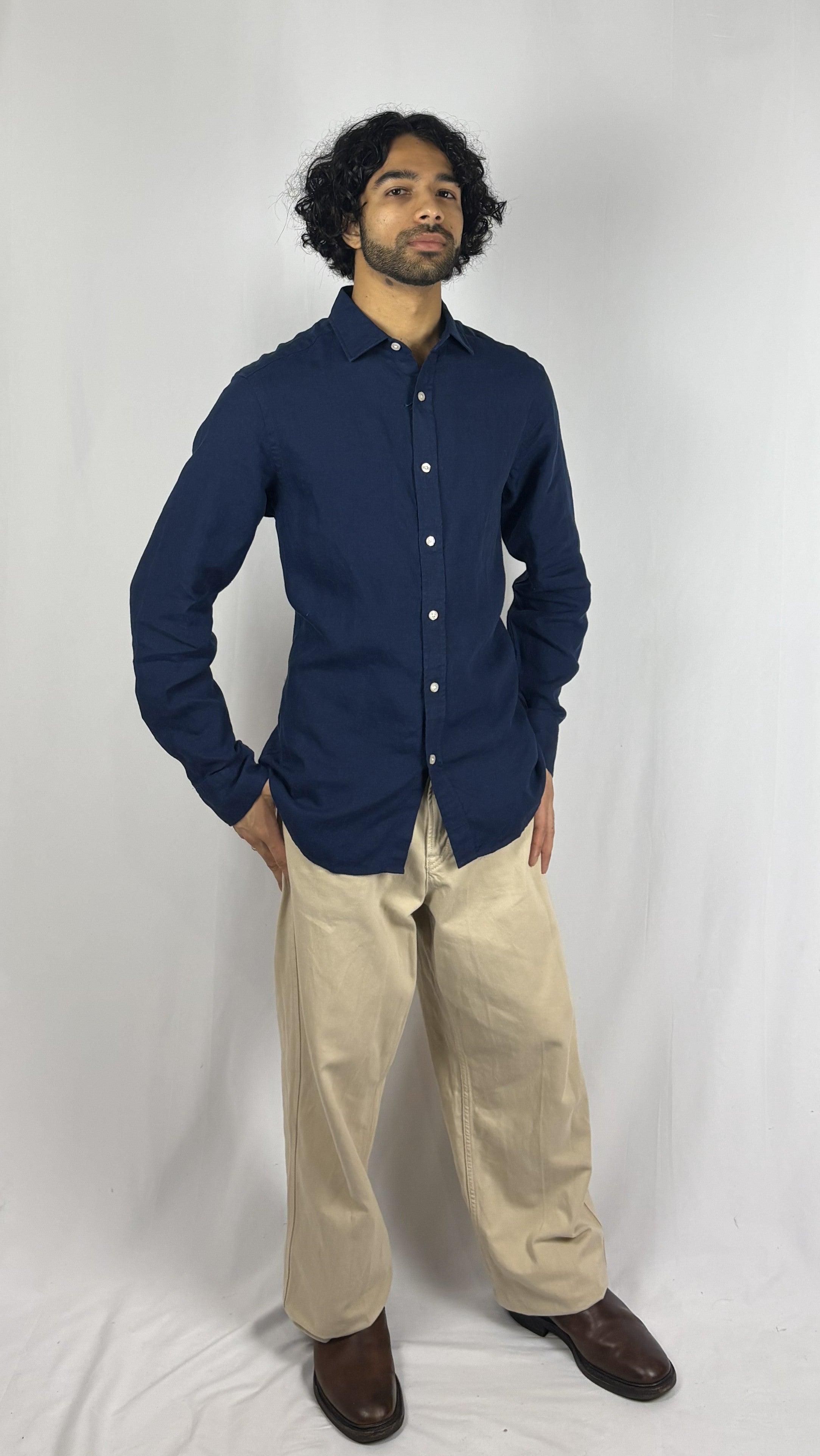 Man wearing a navy blue shirt and beige pants against a white background